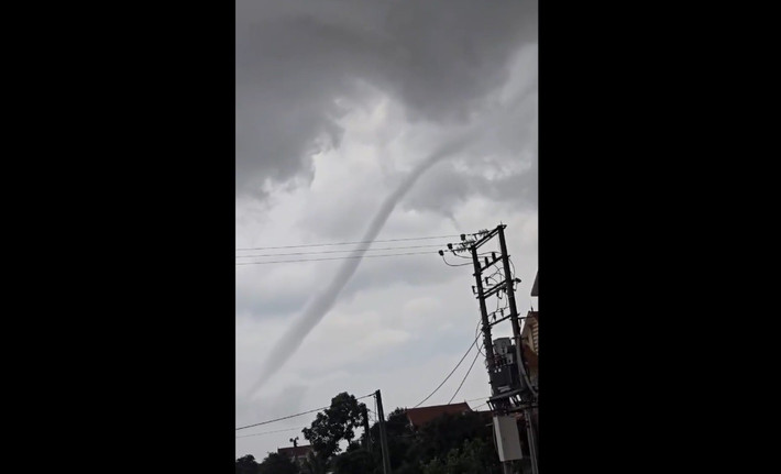 Hiện tượng này kéo dài khoảng 15 phút, với hình dạng đặc trưng là một cột xoáy hình phễu nối từ mặt đất lên một đám mây đen đặc phía trên. Vòi rồng cuộn xoáy dữ dội nhưng nhanh chóng tan biến, không gây thiệt hại về người hay tài sản. Ảnh: Cắt từ clip/Vietnamnet.