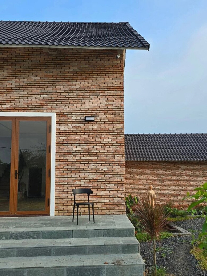 Ngôi nhà chính thiết kế theo phong cách hiện đại nhưng vẫn giữ nét mộc mạc nhờ mảng tường gạch trần không tô trát. Ảnh: FBNV