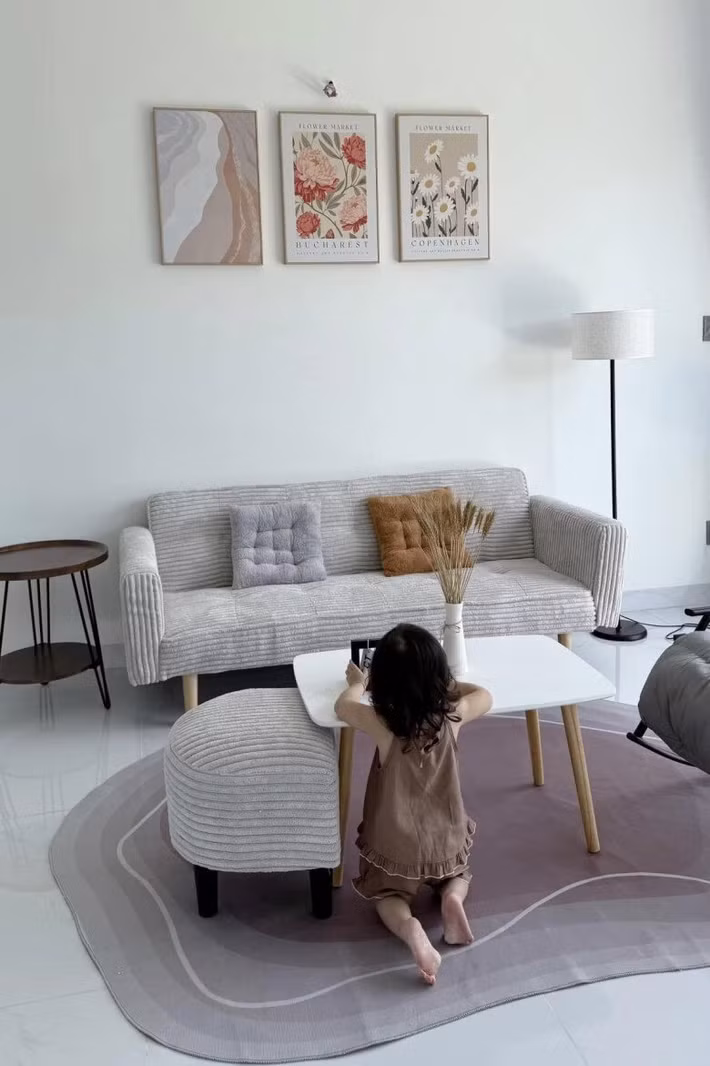 Phòng khách nổi bật với bộ sofa màu xám nhạt kết hợp bàn trà chân gỗ đơn giản. Trên tường treo những bức tranh hoa lá nhẹ nhàng tạo điểm nhấn cho căn phòng. Ảnh: FBNV