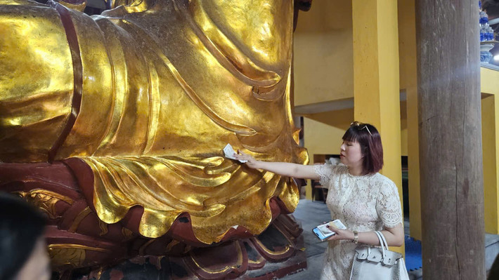 Một người phụ nữ quệt tiền lên tượng Phật lớn trong chùa Tranh.