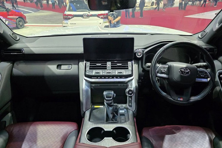 Khoang lái của Toyota Land Cruiser 300 GR Sport kết hợp giữa phong cách sang trọng và tinh thần thể thao. Các chi tiết ốp da màu đen tương phản với đường chỉ đỏ nổi bật, đi kèm logo GR xuất hiện trên vô-lăng, tựa đầu và nút khởi động.