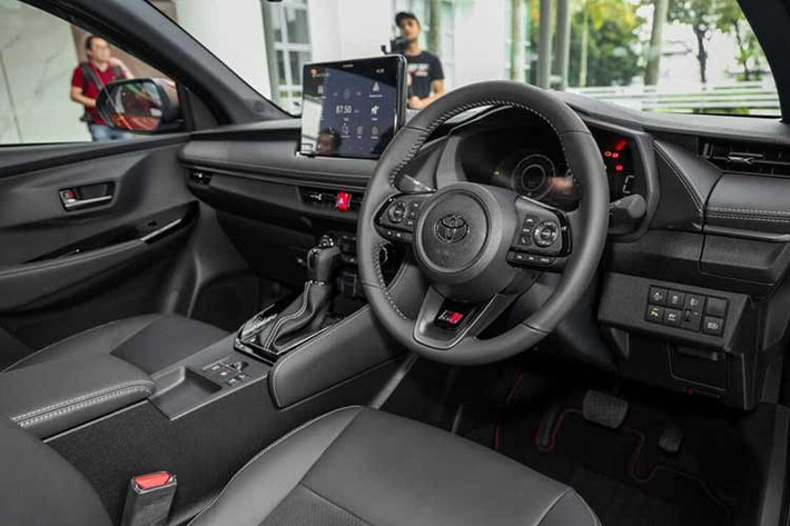 Khoang lái của Vios Hybrid vẫn sử dụng tông màu đen kết hợp đỏ rượu, trang bị bảng táp-lô mềm, ghế da, cùng hệ thống đèn viền 64 màu. Nâng cấp đáng chú ý là màn hình giải trí trung tâm 10,1 inch – lớn hơn bản xăng, hỗ trợ Apple CarPlay/Android Auto không dây, cùng sạc không dây và dàn âm thanh 6 loa.