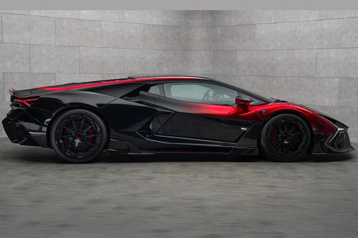 Phần đầu Lamborghini Revuelto Mansory Initiate táo bạo hơn nhờ vào thiết kế khí động học cùng nhiều đường cắt xẻ, kết hợp logo Mansory phát sáng ở nắp capo. Thân xe có điểm nhấn là màu sơn phối đỏ - đen cùng hiệu ứng Ombré.
