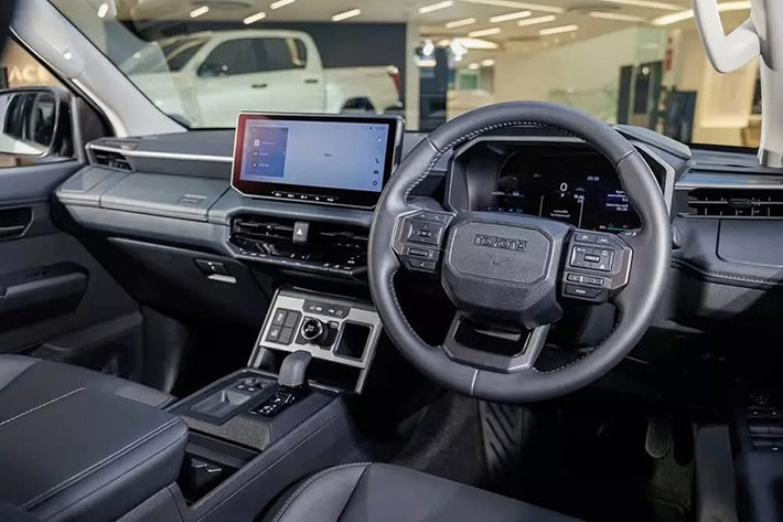 Bên trong, nội thất Hilux 2026 mang thiết kế hiện đại tương tự dòng Land Cruiser, nổi bật với bảng táp-lô trải ngang và cụm màn hình kép 12,3 inch: một cho hệ thống giải trí trung tâm và một cho cụm đồng hồ kỹ thuật số trước vô-lăng. Trang bị tiện nghi được nâng tầm với điều hòa tự động hai vùng, sạc không dây, phanh tay điện tử, nhiều cổng USB, nội thất bọc da Softex và hệ thống âm thanh 8 loa.