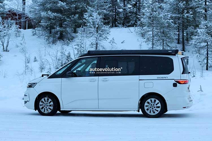 Trong ảnh, chiếc xe Volkswagen Multivan T7 2027 nguyên mẫu được ngụy trang với các hình dán Ocean trên phần thân sau, đang được thử nghiệm trong điều kiện thời tiết lạnh giá ở Thụy Điển với đèn pha hoàn toàn mới, lớn hơn một chút so với đèn pha của mẫu California tiền nhiệm.