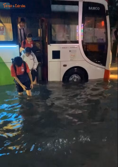 Học sinh phải lội trên đường ngập sau khi xuống từ xe ô tô đưa rước.