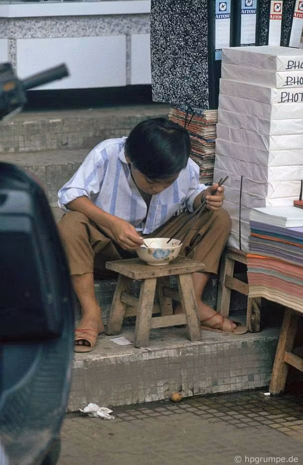 Một cậu bé ngồi ăn cạnh quầy bán giấy photo ở TP HCM.