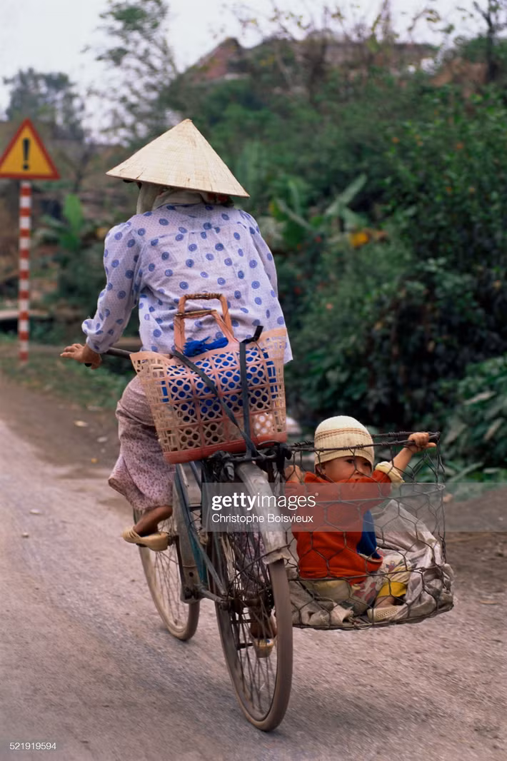 Bà mẹ chở con bằng chiếc sọt sắt gắn sau xe đạp.