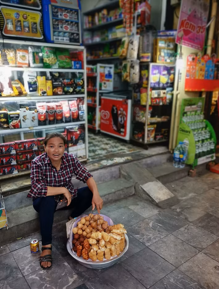 "Cô gái donut" bên ngoài một cửa hàng tạp hóa Hà Nội. Trong khay đồ của cô là các loạt bánh rán truyền thống. Ảnh: Cowyeow / Flickr.